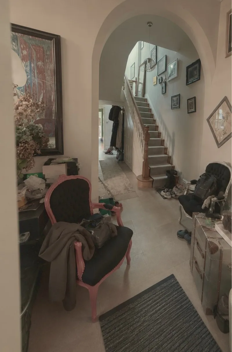 A hallway with coats, shoes, boxes and bags stacked along it